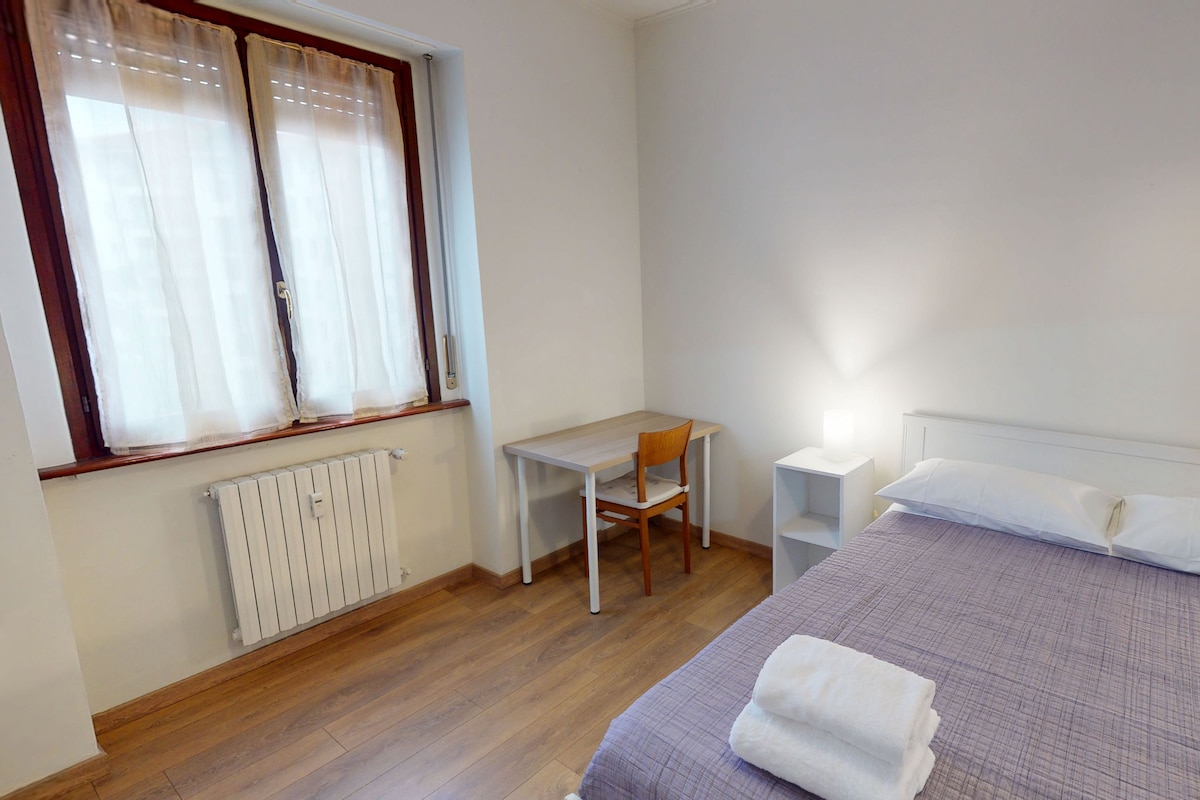 A bedroom with a bed, a desk, a chair, and a radiator.