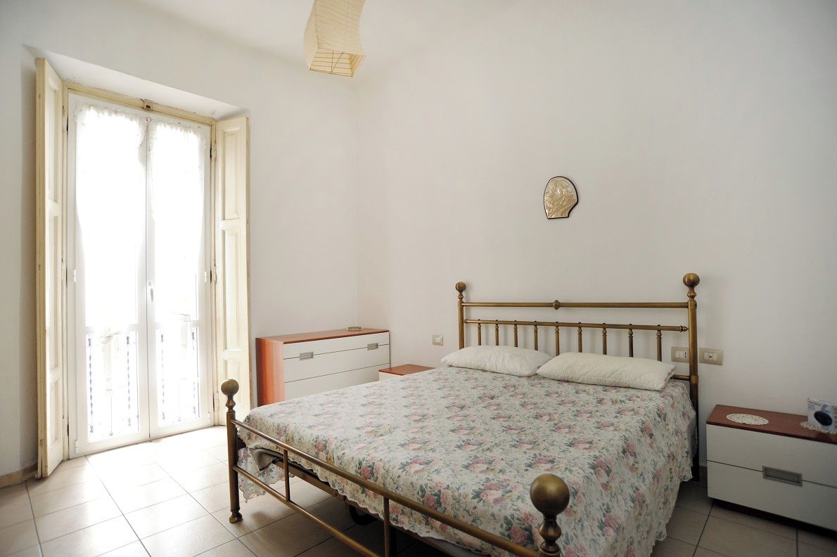 A bedroom with a bed, a nightstand, a dresser, and a window with curtains.