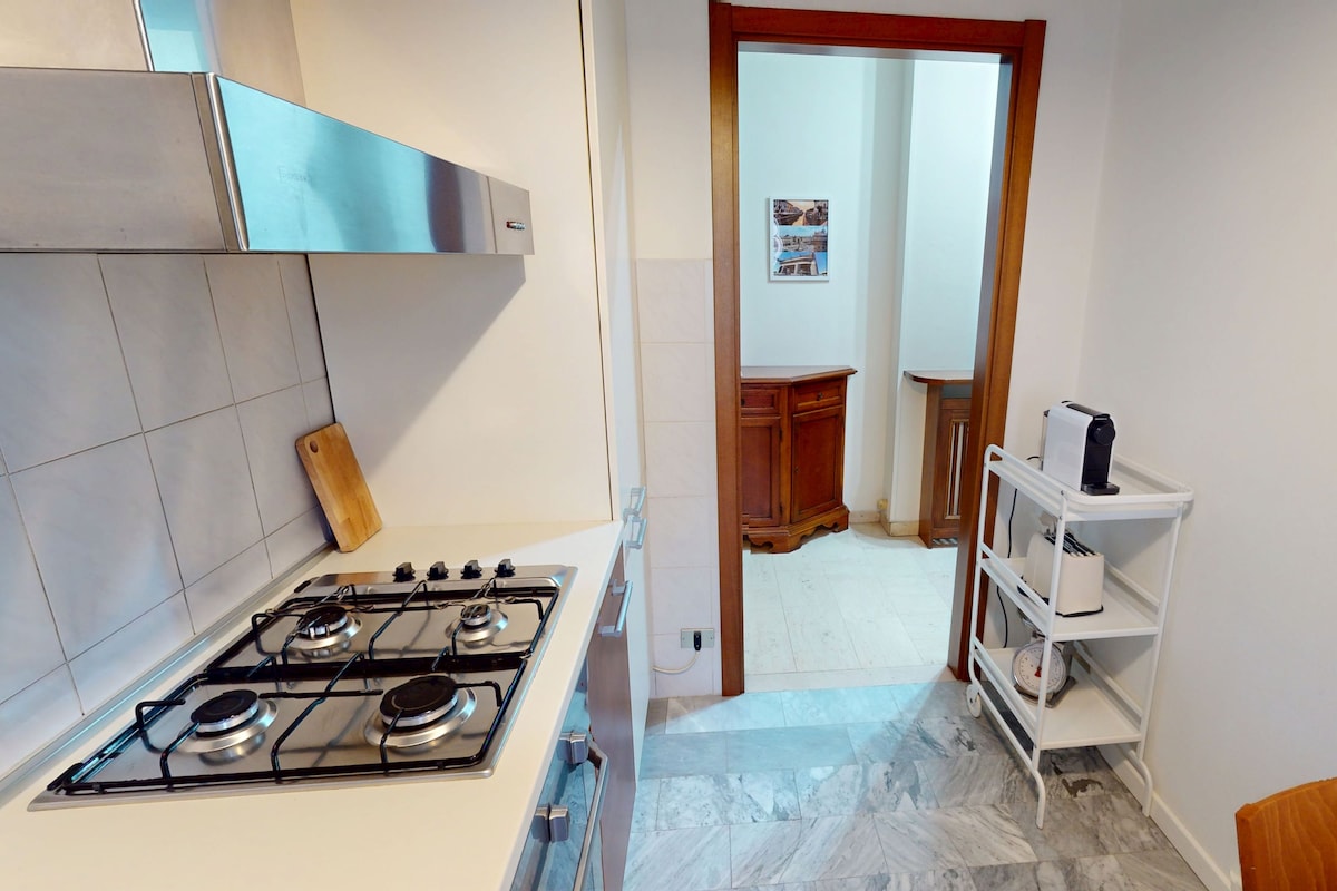 A compact kitchen with a gas stove, a wooden cutting board, and a white shelf unit.