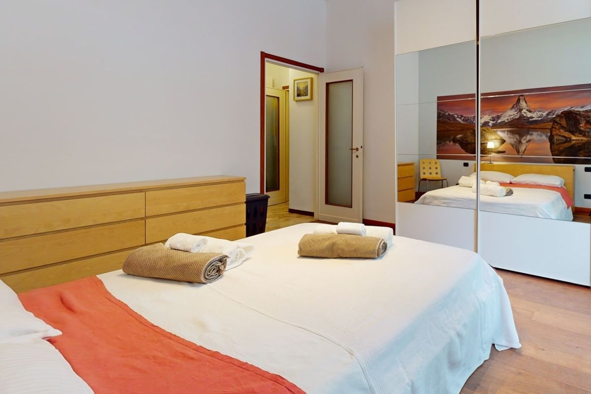 A hotel room with a bed, a wardrobe, a mirror, and a painting on the wall.