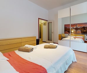 A hotel room with a bed, a wardrobe, a mirror, and a painting on the wall.