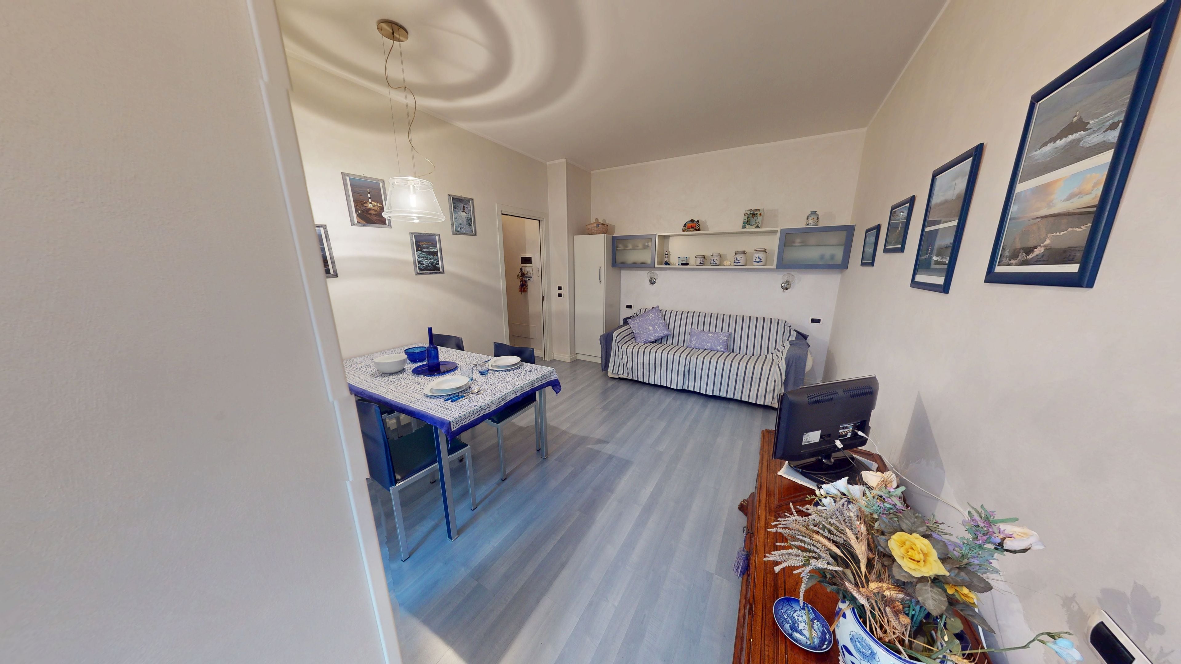 Un comedor con una mesa dispuesta para dos personas, un sofá y un televisor sobre un mueble de madera.