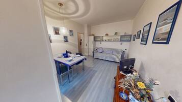 Un coin repas avec une table dressée pour deux personnes, un canapé et un téléviseur posé sur un meuble en bois.