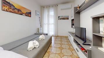 Ein Hotelzimmer mit einem Bett, einem Fernseher, einem Bücherregal und einem Fenster mit Vorhängen.