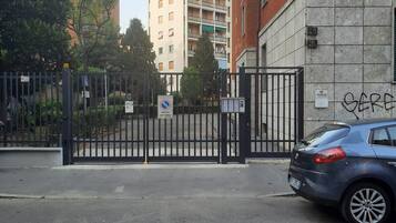 Une entrée fermée par un portail donnant accès à un quartier résidentiel, avec une voiture bleue garée à proximité.
