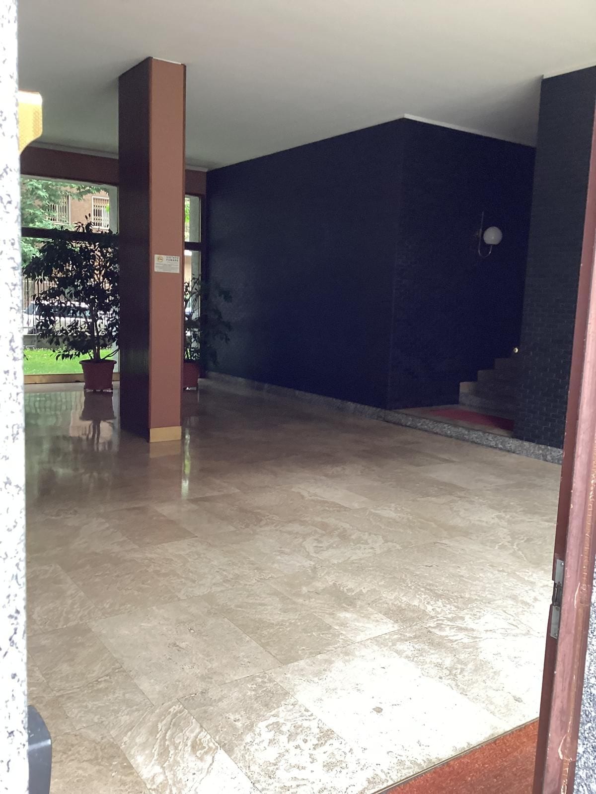 Un'ampia area interna con pavimento piastrellato, una pianta in vaso e una scala che conduce a un livello superiore.