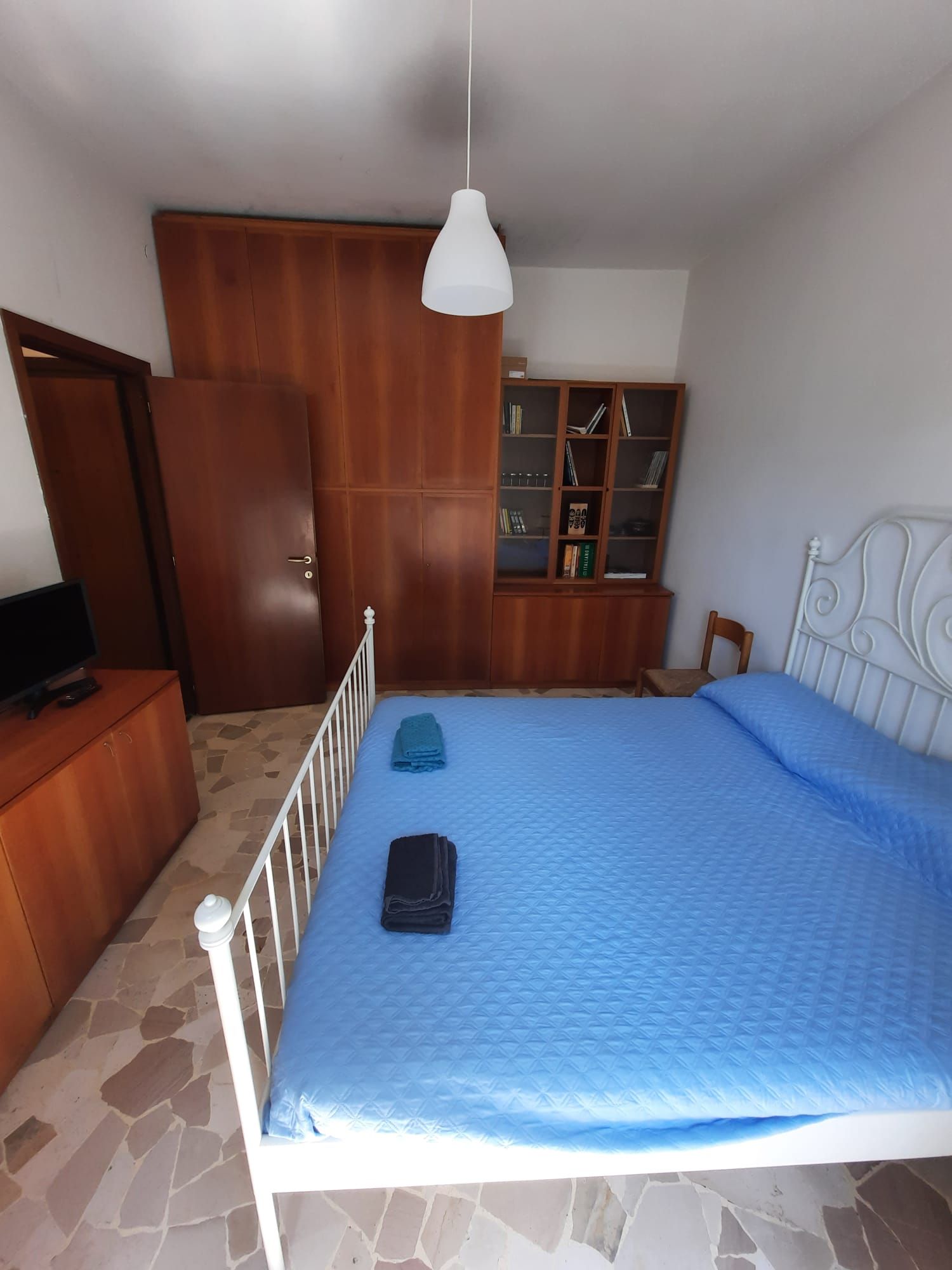 Quarto com cama, guarda-roupa, estante de livros e televisão.