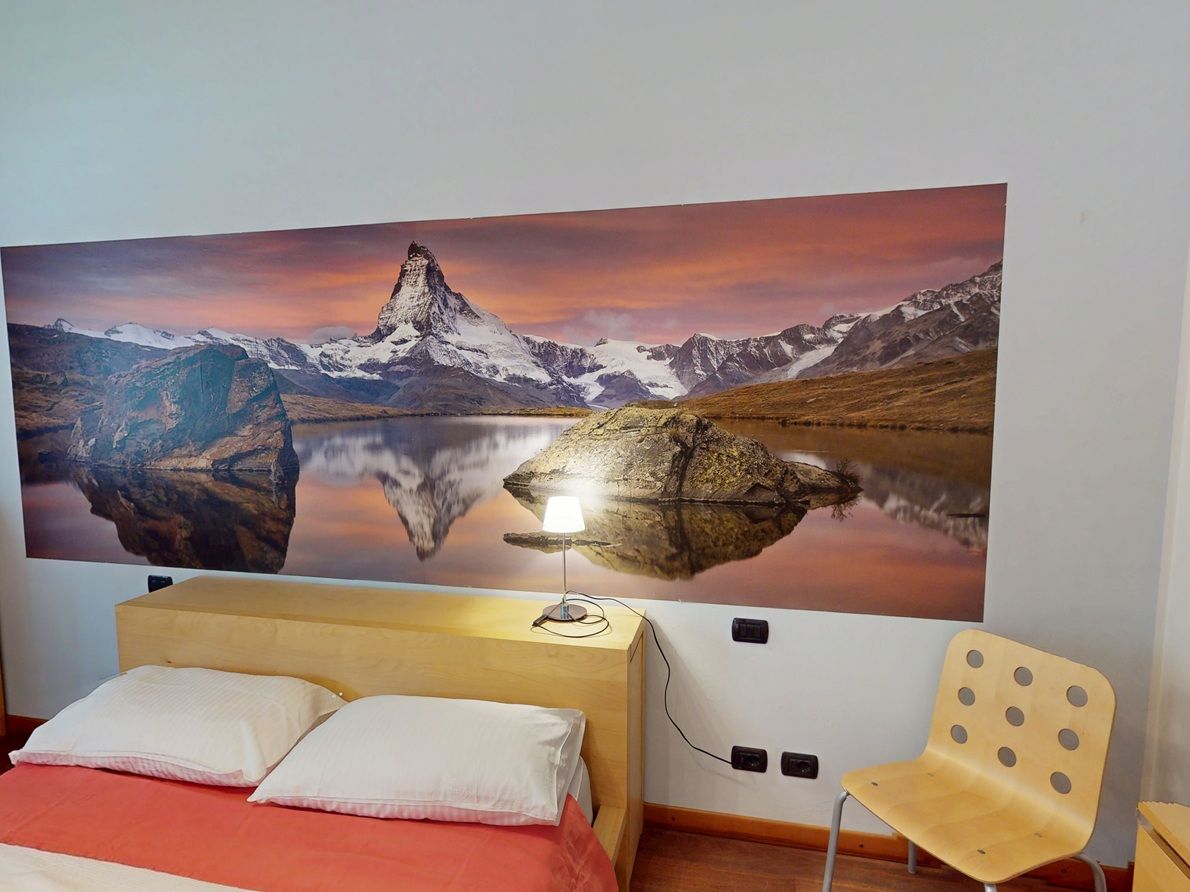 A room with a bed, a chair, and a large wall-mounted painting of a mountain landscape.