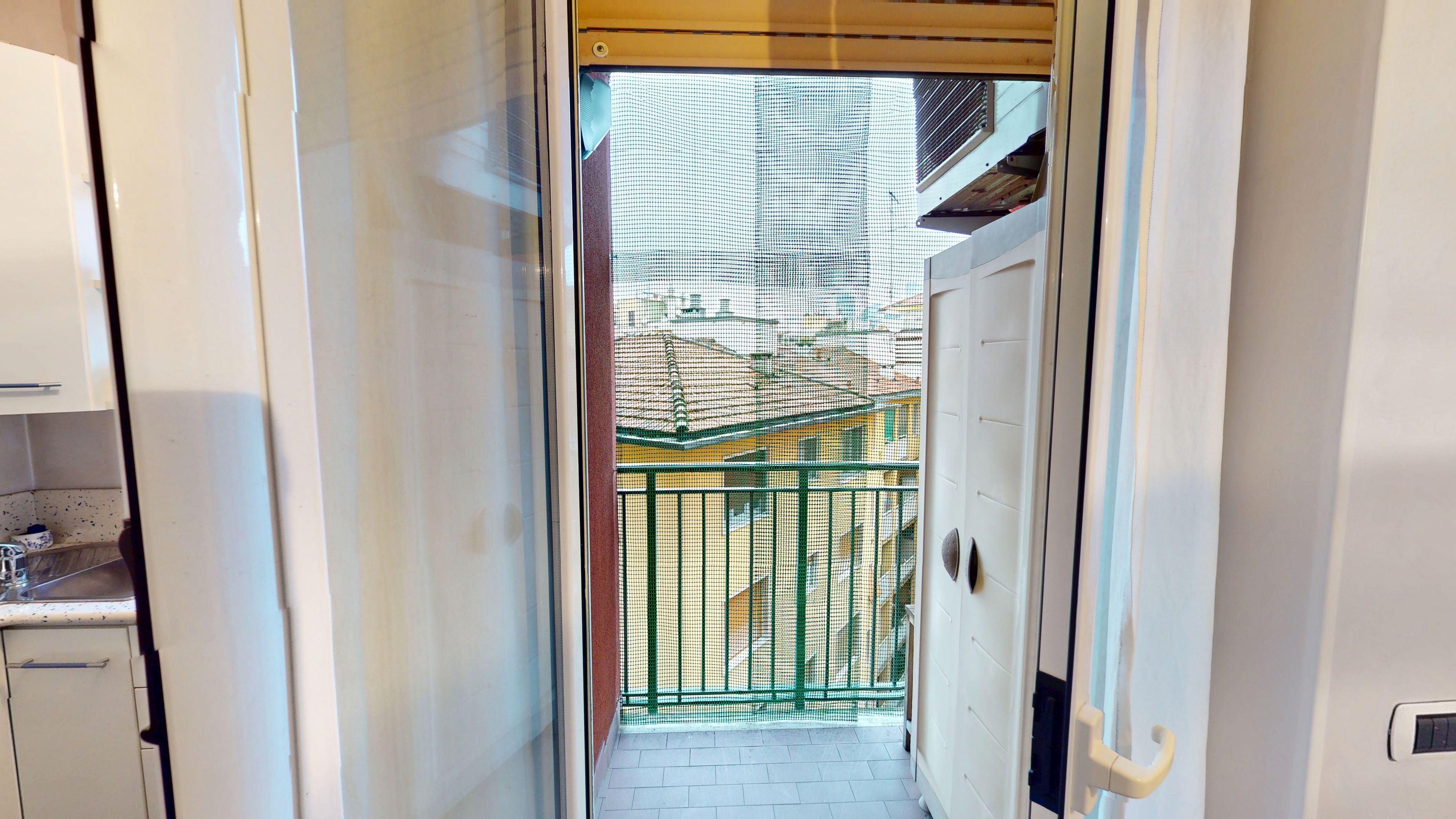 A narrow hallway with a door leading to a balcony with a green metal railing.