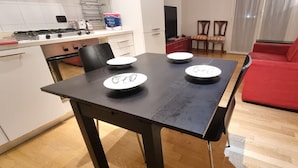 A dining area with a black table, four white plates, and a red sofa. - Come a Casa Tua Milano (Milano)