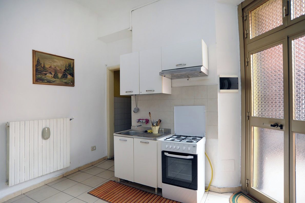 Une cuisine de taille réduite, avec des meubles blancs, une cuisinière à gaz et un four encastré.