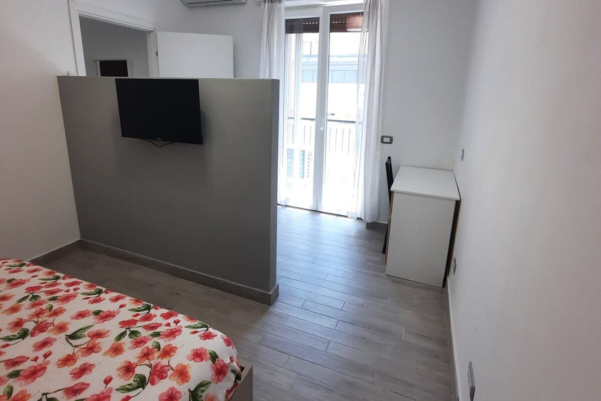 A hotel room with a bed, a television, a desk, and a window with curtains.