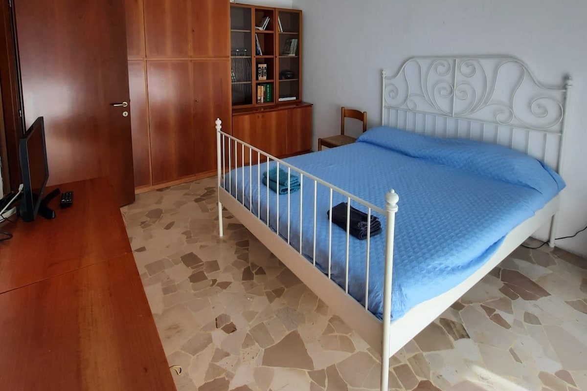 A bedroom with a bed, wardrobe, desk, and a hanging light fixture.