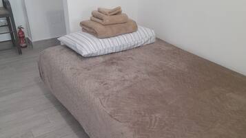 Ein Einzelbett mit einer gemusterten Bettdecke und einer umgelegten Wolldecke.