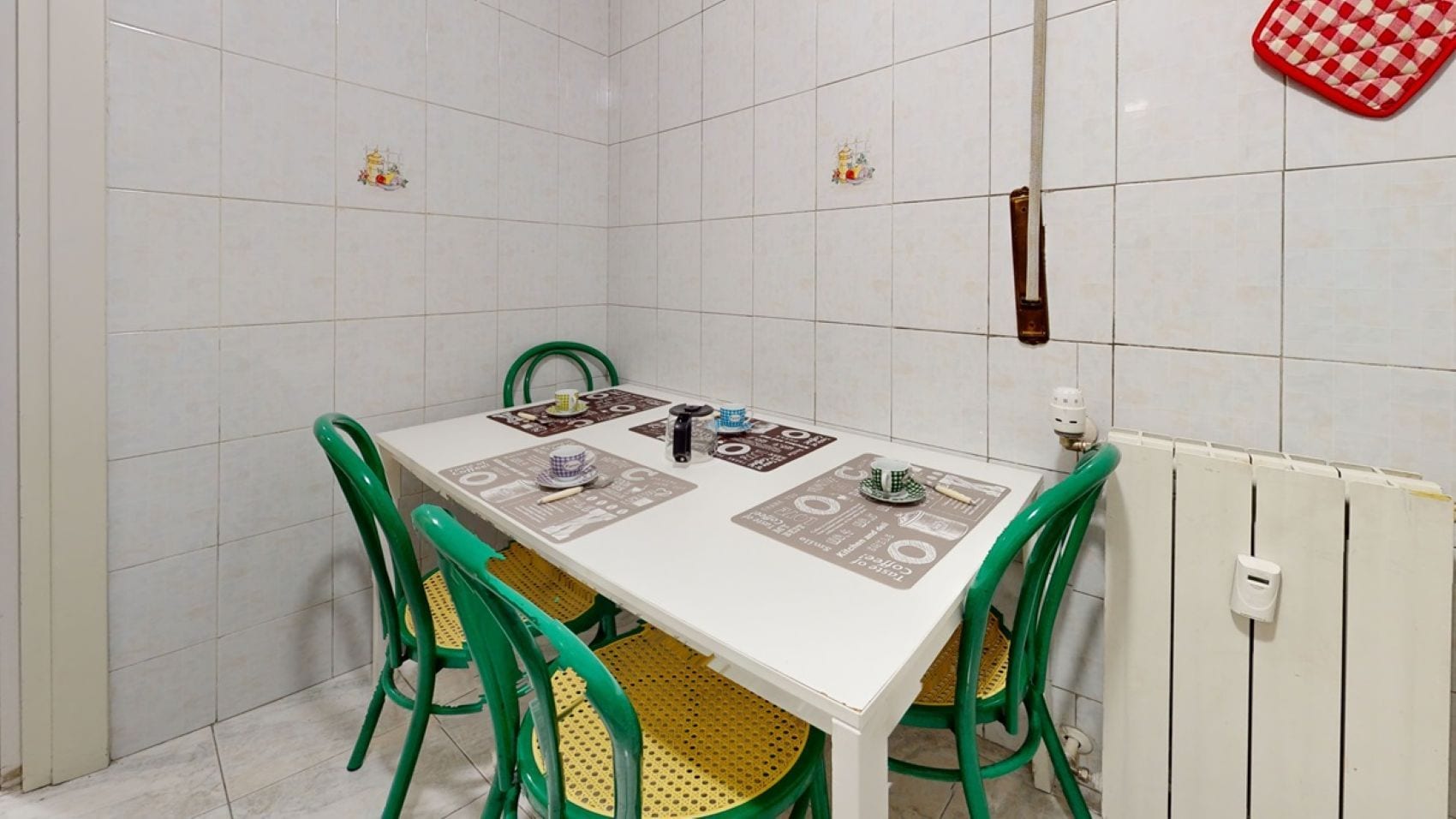 Uma área de refeições com uma mesa branca, cadeiras verdes e um radiador.