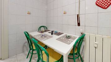 Uma área de refeições com uma mesa branca, cadeiras verdes e um radiador.