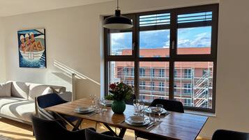 A dining area with a table set for four, a sofa, a painting, and a large window with a view of buildings.