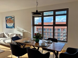 Ein Essbereich mit einem Tisch für vier Personen, einer Couch, einem Gemälde und einem großen Fenster mit Blick auf Gebäude.