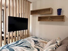 A bedroom with a bed, a mounted TV, wooden slats, and two wooden shelves with decorative items.