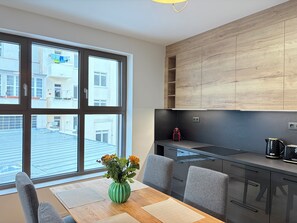 A modern kitchen with a large window, a dining table with chairs, and a vase with flowers.