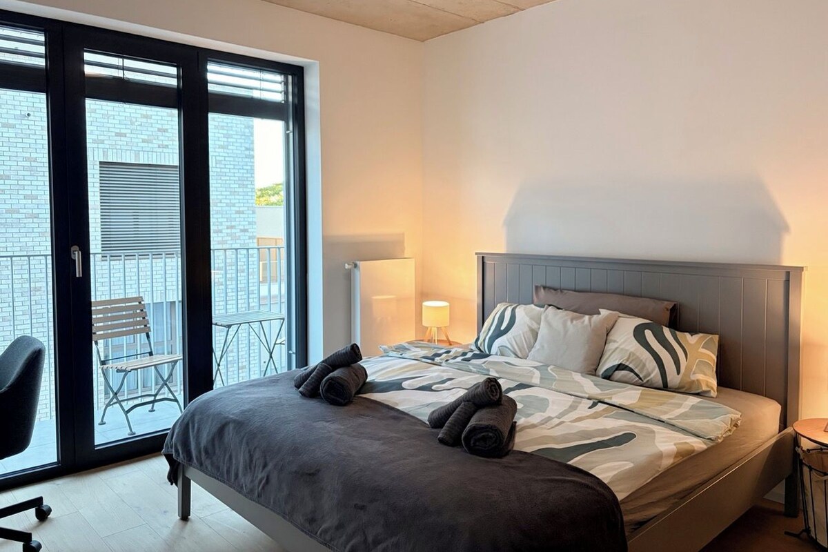 A modern hotel room with a bed, a chair, a lamp, and a balcony with a chair.