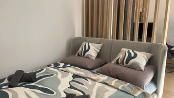 A modern bedroom with a sofa bed, patterned bedding, and a wooden partition.