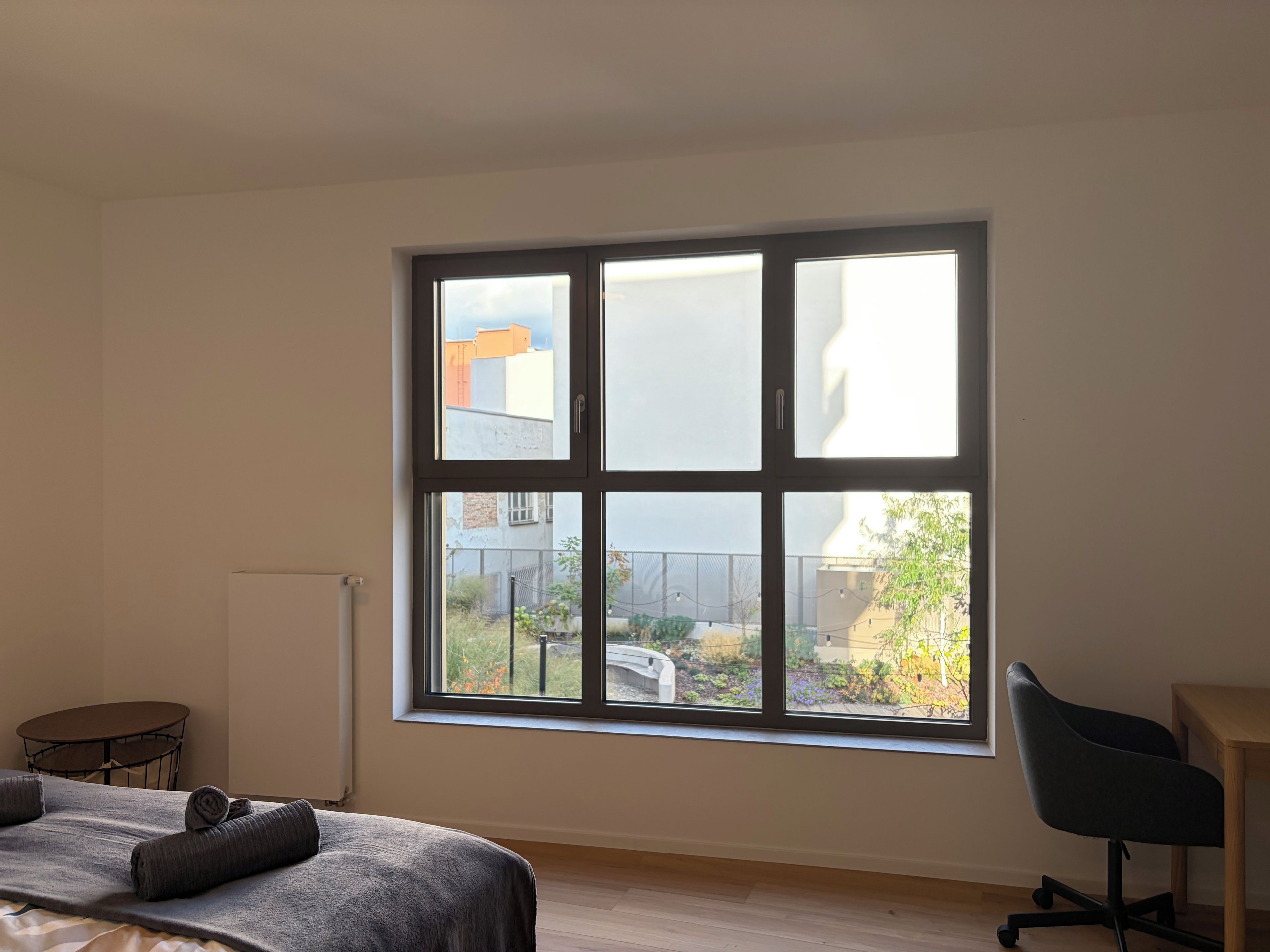 Une pièce avec une grande fenêtre, un lit, une chaise et une petite table.