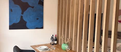 A dining area with a wooden table set for two, a modern chair, a wall-mounted abstract painting, and a wooden partition.