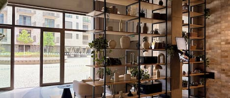 A modern interior with a large window, a central seating area, and a multi-tiered shelving unit filled with decorative items.