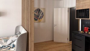 A modern bedroom with a bed, a wooden partition, a door, and a kitchenette with a coffee machine.