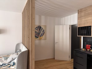 Une chambre moderne comprenant un lit, une cloison en bois, une porte et un coin cuisine équipé d’une machine à café.