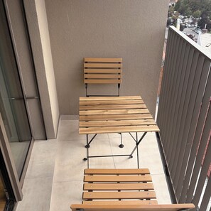 A balcony with a wooden table and bench, a view of the street, and a building in the background.