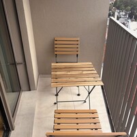 Un balcón con una mesa y banco de madera, vista a la calle y un edificio al fondo.