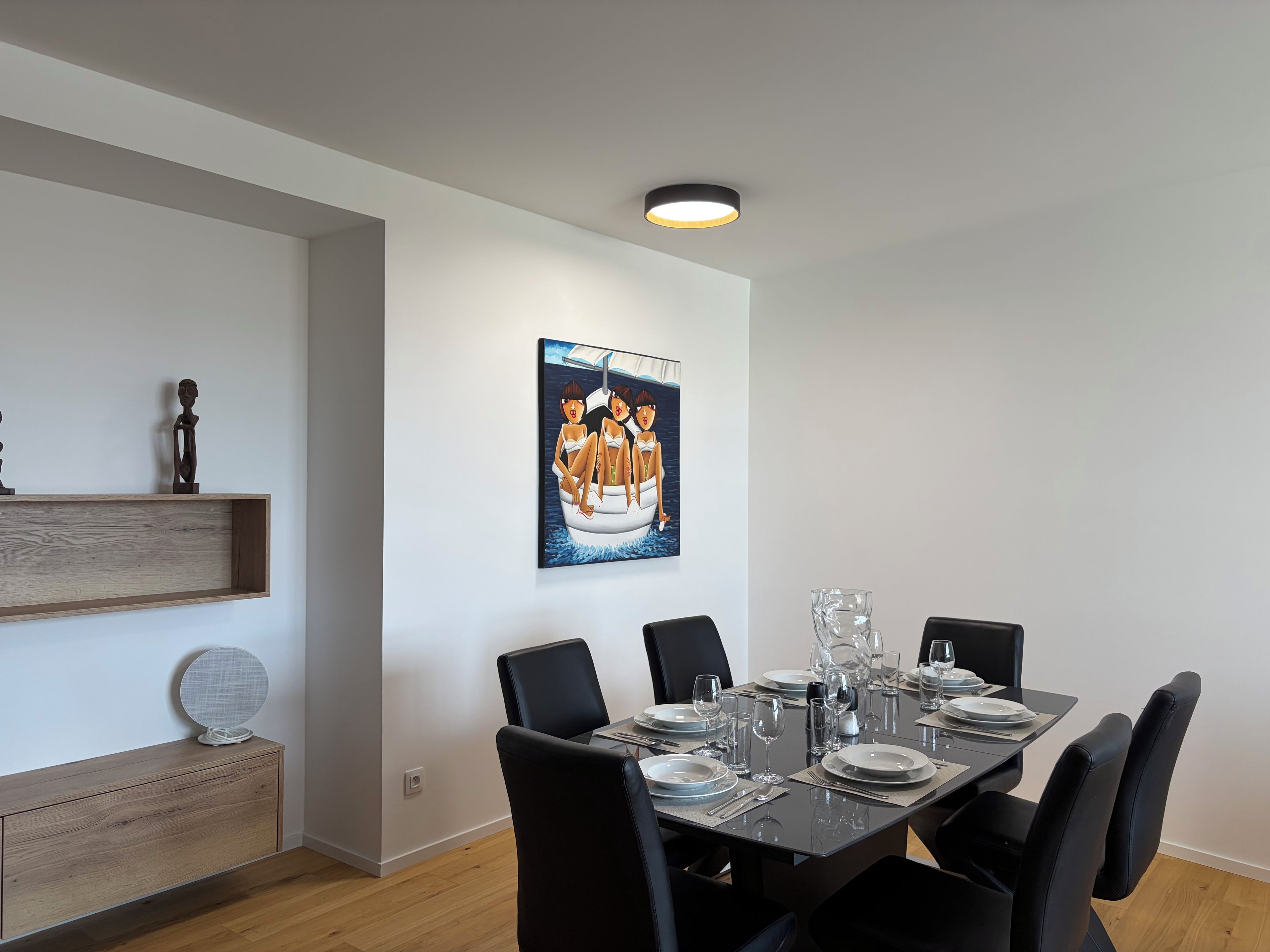 Comedor con una mesa rectangular dispuesta para seis comensales, sillas negras y un cuadro colgado en la pared.