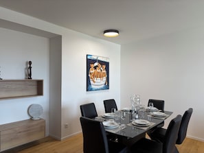Comedor con una mesa rectangular dispuesta para seis comensales, sillas negras y un cuadro colgado en la pared.