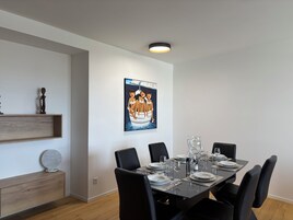 Comedor con una mesa rectangular dispuesta para seis comensales, sillas negras y un cuadro colgado en la pared.