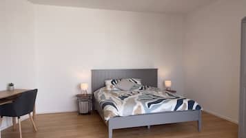 A bedroom with a bed, bedside tables, a desk, and a chair.