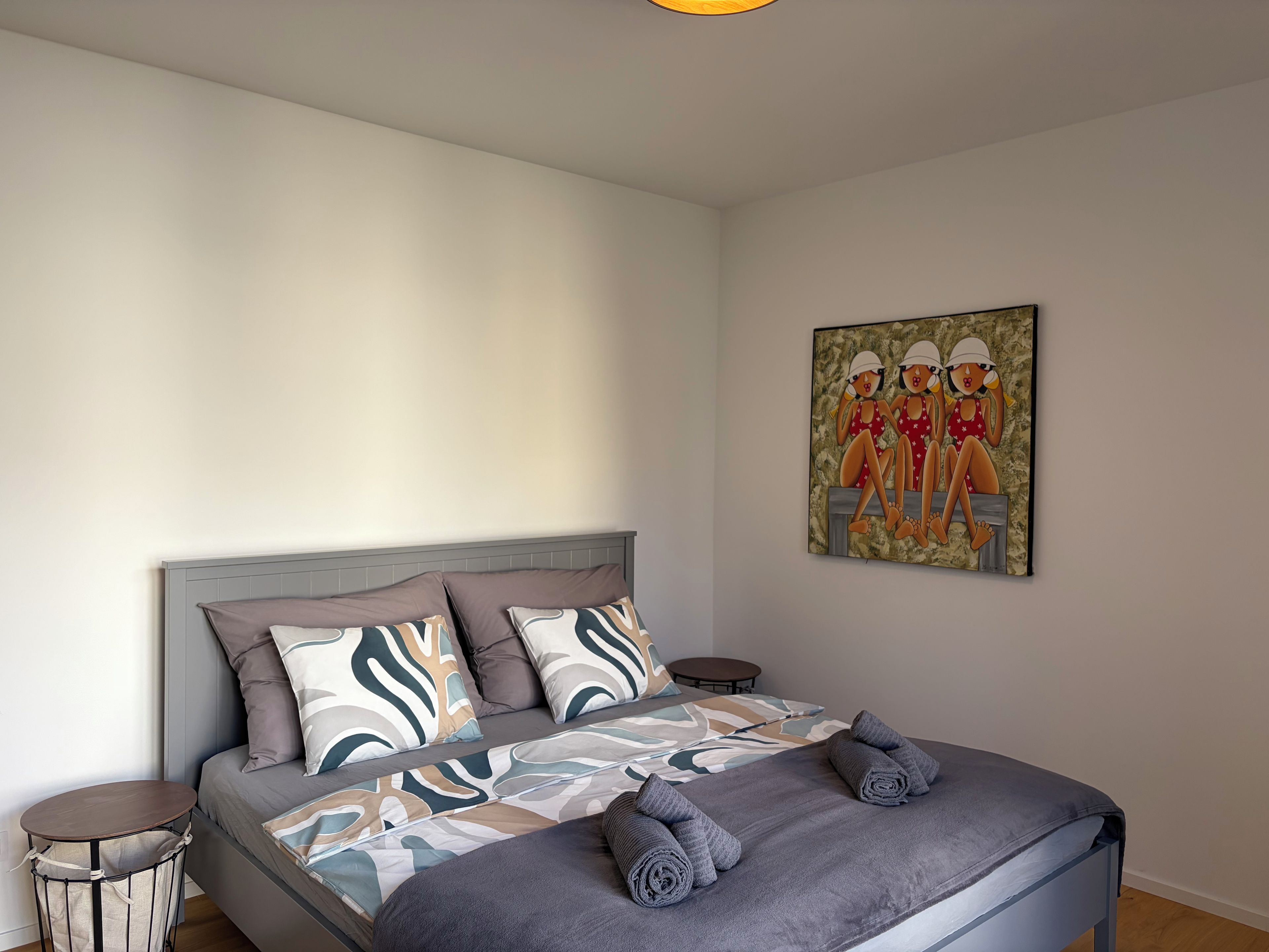 Un dormitorio con una cama, almohadas, una mesa redonda y un cuadro en la pared.