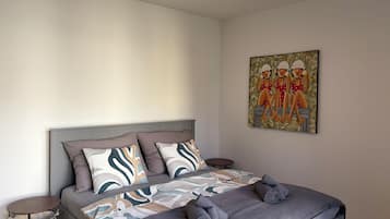 Un dormitorio con una cama, almohadas, una mesa redonda y un cuadro en la pared.