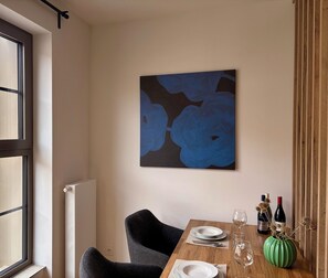 Ein Essbereich mit einem Tisch für zwei Personen, einem Gemälde an der Wand und einem Fenster mit Jalousien.