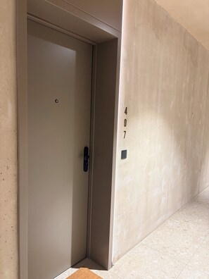 A door with a numeric keypad, a textured wall, and a tiled floor.