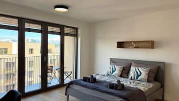 A bedroom with a bed, a nightstand, a chair, a balcony, and a city view.