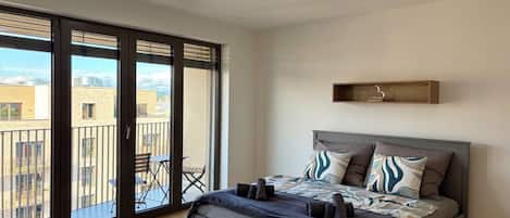 Une chambre avec un lit, une table de chevet, une chaise, un balcon et une vue sur la ville.