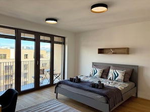 A bedroom with a bed, a nightstand, a chair, a balcony, and a city view.