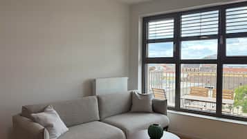 A modern living room with a grey sofa, a small round table, and a large window with a view of buildings.