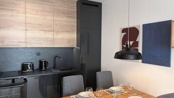 A modern kitchen with a dining area, featuring a wooden countertop, a black refrigerator, and a dining table set for four.