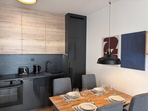 A modern kitchen with a dining area, featuring a wooden countertop, a black refrigerator, and a dining table set for four.