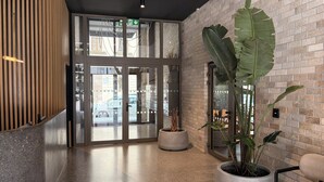 A lobby with a reception desk, a large potted plant, and a glass door leading outside.