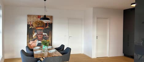 A modern dining area with a wooden table, grey upholstered chairs, and a large painting above.