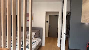 A bedroom with a bed, wooden floor, and a door leading to another room.